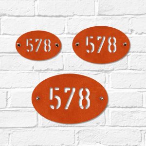 Small, medium & large modern oval metal house number in rusted industrial look Corten weathering steel on a white brick wall