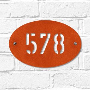 Modern oval metal house number in rusted industrial look Corten weathering steel on a white brick wall