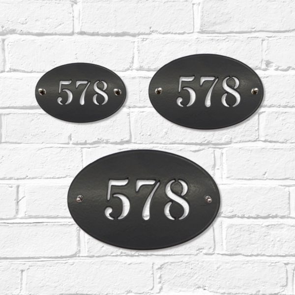 Small, medium and large classic oval metal house number signs in black steel on a white brick wall