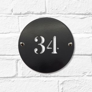 Classic round metal house number sign in black steel on a white brick wall