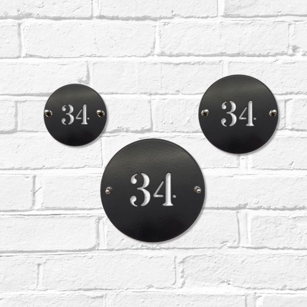 Small, medium and large classic round metal house number signs in black steel on a white brick wall