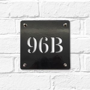 Classic square metal house number sign in black steel on a white brick wall
