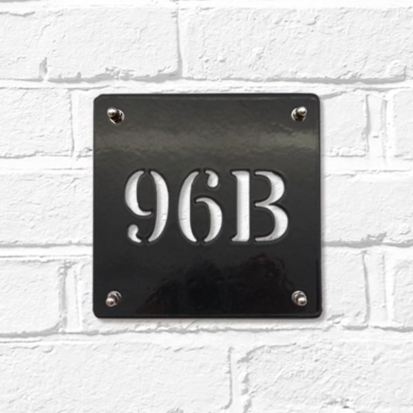 Classic square metal house number sign in black steel on a white brick wall