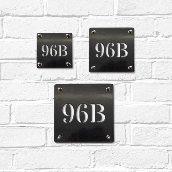 Small, medium and large classic square metal house number signs in black steel on a white brick wall