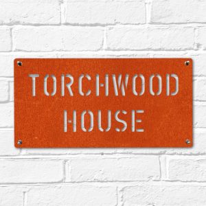 Modern rectangular metal house name plate sign in rusted industrial look Corten weathering steel on a white brick wall
