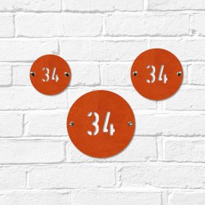 Small, medium & large modern round metal house number in rusted industrial look Corten weathering steel on a white brick wall