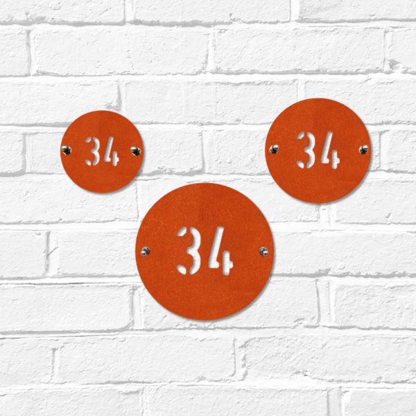 Small, medium & large modern round metal house number in rusted industrial look Corten weathering steel on a white brick wall