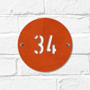 Modern round metal house number in rusted industrial look Corten weathering steel on a white brick wall