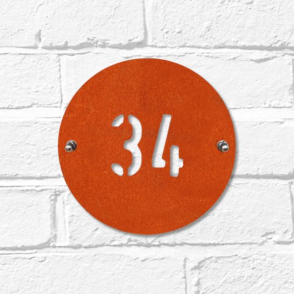 Modern round metal house number in rusted industrial look Corten weathering steel on a white brick wall