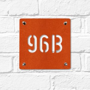 Modern square metal house number in rusted industrial look Corten weathering steel on a white brick wall