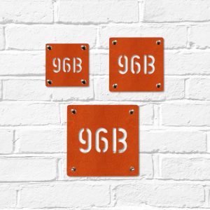 Small, medium & large modern square metal house number in rusted industrial look Corten weathering steel on a white brick wall