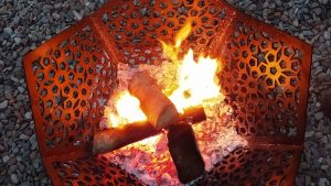 A lit black Star of Morocco Fire Pit BBQ and Ground Guard burning wood on a summer's evening