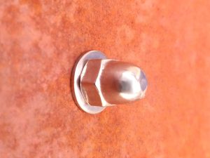 Closeup of stainless steel dome head sign fixing kit in use with COR-TEN weathering steel