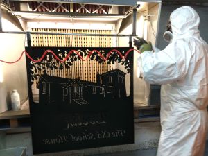 Applying the fine textured cast iron effect powder coat to the front layer of the sign